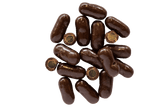 Bullets Dark Chocolate Coated in small scattered pile, some cut open to expose licorice centre.