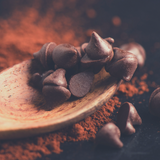 Close up of Callebaut Dark Chocolate callets on end of wooden spoon, sitting in cocoa powder..