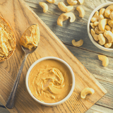 Cashew Butter in round ceramic bowl and heaped on tablespoon. Sitting on timber chopping board.