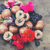 Close up of pile of Milk Chocolate Cherries, some sliced in half to expose cherry centre. Decorated with edible flowers.