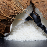 Close up of heaped pile of Desiccated Coconut under cracked open coconut, on black background.