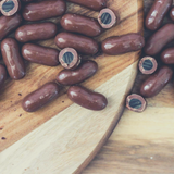 Close up of Dark Chocolate Coated Bullets scattered on timber boards. Some cut open to expose the licorice centre.