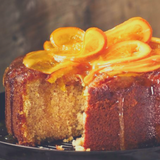 Cake with one slice taken out. Topped with Glace Orange slices and drizzled syrup.