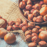 Overflowing bowl of raw hazelnuts, mixed with whole hazelnuts in their shell.