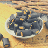 Dutch Salmiak Rocks in bowl sitting on timber chopping board, next to liquorice root.