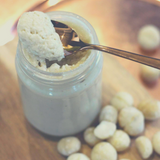 Small glass jar filled with Macadamia Butter being scooped out with copper spoon.