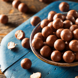 Bowl of Chocolate Malt Balls on blue timber board with broken malt balls scattered around.