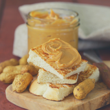 Smooth Peanut Butter spread on toasted white bread, sitting in front of glass peanut butter jar.