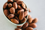 Close up of small bowl of Almonds Tamari on light grey background.