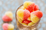 Close up of Sour Peach Hearts in round glass on light orange background.