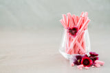 Glass full of Musk Sticks, decorated with pink edible flowers. Concrete background.