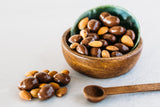 Milk Chocolate Almonds in green and timber bowl. Small timber spoon and cluster of almonds sitting next to the bowl on concrete background.