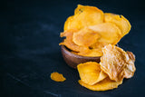 Vibrant Dried Mango in overflowing out of timber bowl, on black stone benchtop.