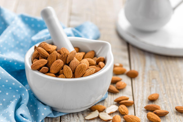 Small white bowl full of almonds on a table with a blue tea towel