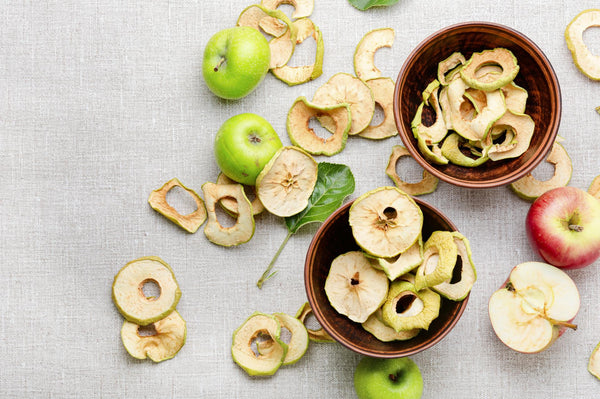Dried apple rings on a table with fresh apples and bowls