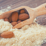 Timber spoon full of raw whole almonds sitting in a handful of Blanched Almond Meal.