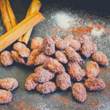 Close up of Cinnamon Almonds dusted with sugar, sitting next to cinnamon sticks. 