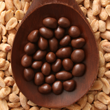 Dark Chocolate Peanuts on timber spoon, sitting on top of bulk dry-roasted peanuts.