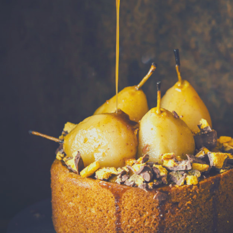 Close up of cake on dark background. Topped with whole baby Glace Pears, drizzled in caramel. 