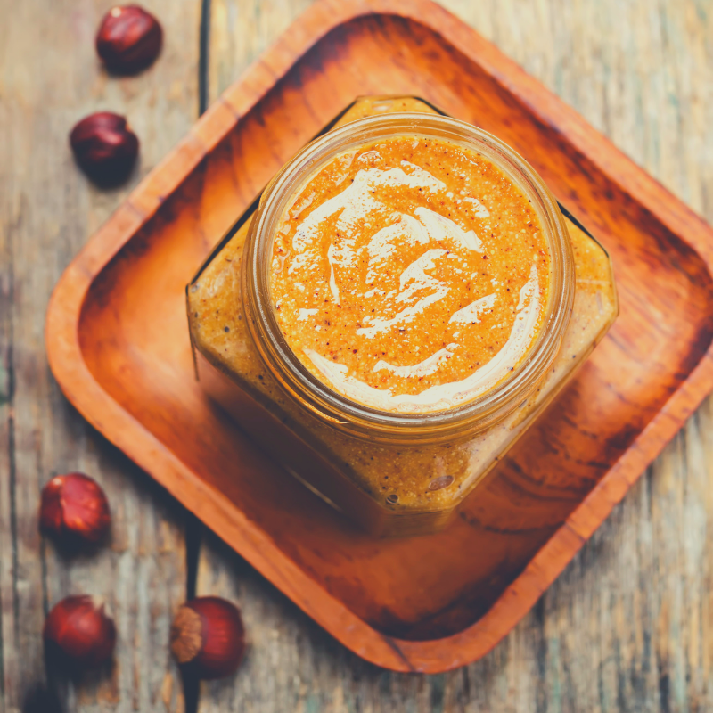 Glass jar full of Hazelnut Butter sitting on square timber tray.