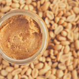 Close up of Crunchy Peanut Butter in glass jar, sitting on bulk peanuts.