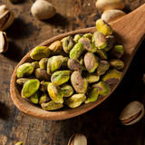 Raw Pistachio nuts on timber serving spoon, on rustic timber background.