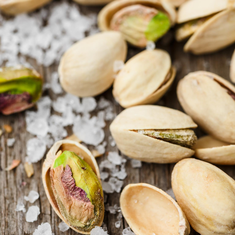 Close up of Pistachio Nuts Roasted and Salted on timber background with salt crystals. 
