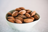 Close up of teardrop shaped, ceramic bowl full of Smoked Almonds, on light grey background.