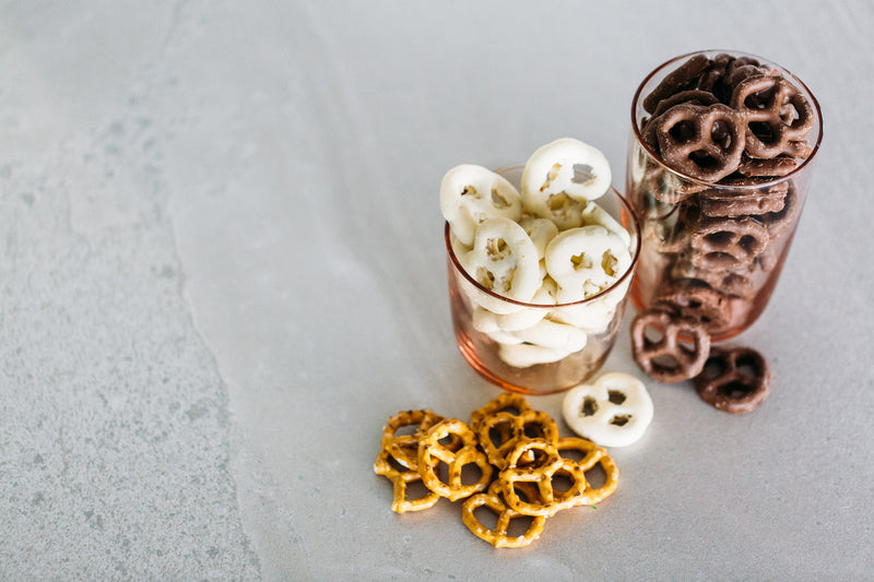 Milk Chocolate Pretzels and Yoghurt Coated Pretzels in glasses, on concrete background.