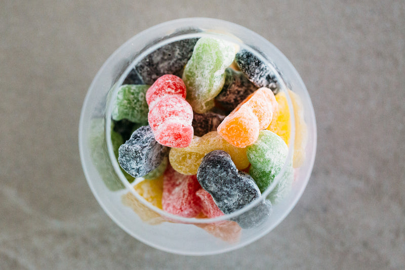 Close up of English Dusted Jelly Babies in glass jar on a light grey background.