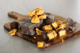 Milk Chocolate Honeycomb pieces with large chunks of milk chocolate, sitting on timber serving board, concrete background.