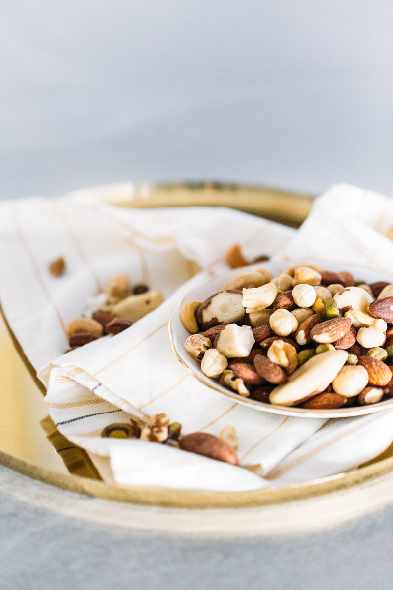 Plate of Mixed Raw Nuts Deluxe sitting on ivory striped napkin and brass tray.