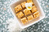 Toasted Mallows in square white bowl, sitting on terazzo background with shredded coconut scattered nearby. 