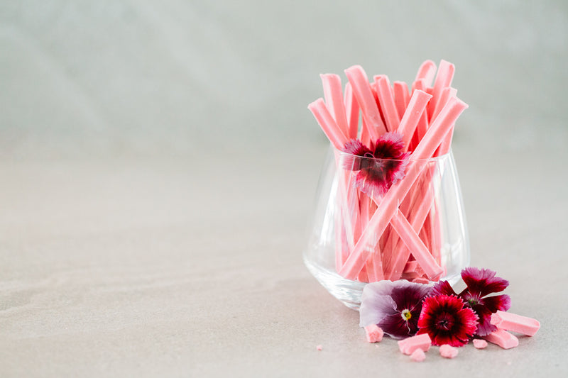 Glass full of Musk Sticks, decorated with pink edible flowers. Concrete background. 