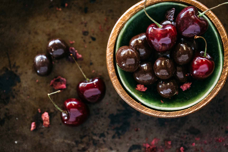 Round green and timber bowl full of red cherries and Dark Chocolate Cherries, on dark background.