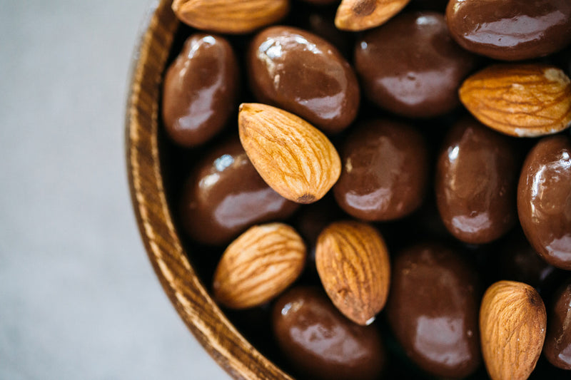 Close up of bowl of Dark Chocolate Almonds with raw almonds scattered on top.