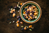 Cranberry Trail Mix in green & timber bowl, sitting next to scattered trail mix on dark background.