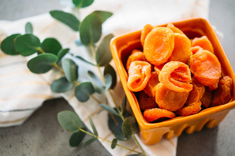 Australian Dried Apricots in vibrant orange ceramic berry container, with sprig of gum leaf and white tea towel in the background.