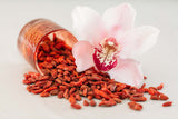 Organic Goji Berries spilling out of red glass onto pale pink background.