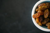 Close up of Organic Sultanas in small bowl on black background.