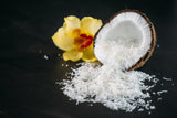 Shredded Coconut Threads spilling out of half coconut shell. Sitting next to a yellow orchid on black background.