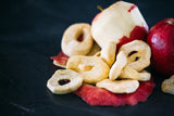 Dried Apple Rings sitting in amongst peeled red apples, on a black background.