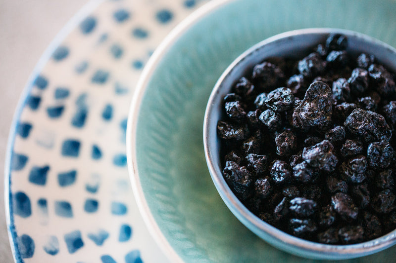 Dried Blueberries sitting in small blue bowl at the centre of 3 ceramic bowls in different shade of blue.