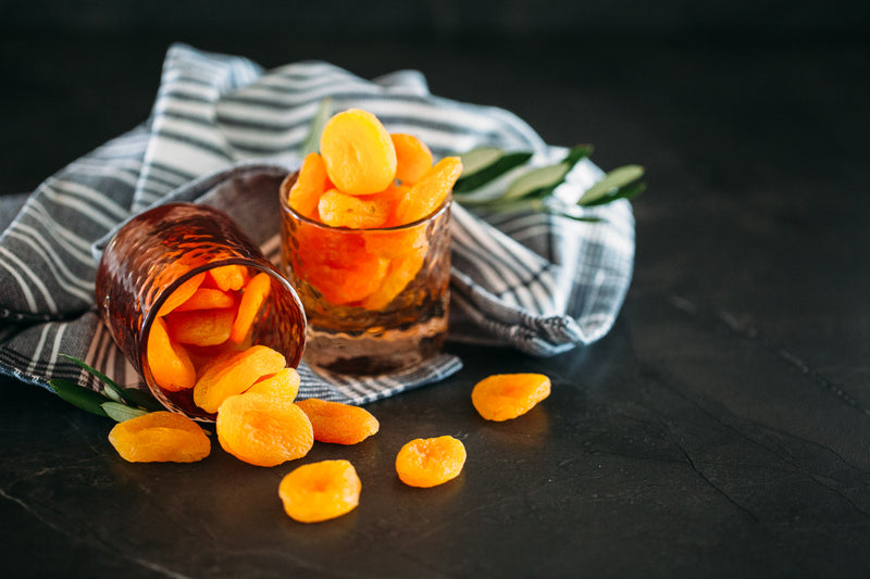 Turkish Apricots in small orange glass jars, sitting on blue cloth with black background.